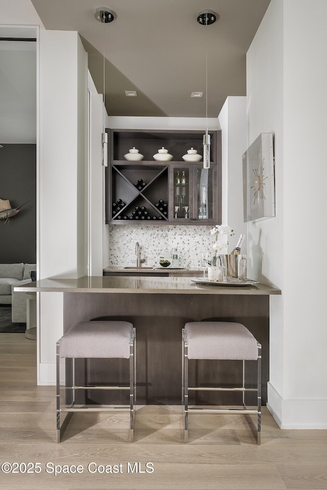 bar featuring hanging light fixtures, tasteful backsplash, light wood-type flooring, and indoor wet bar