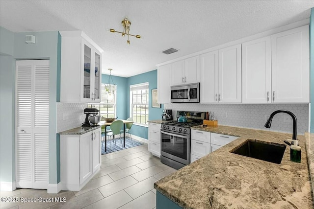 kitchen with light stone counters, a sink, visible vents, white cabinets, and appliances with stainless steel finishes