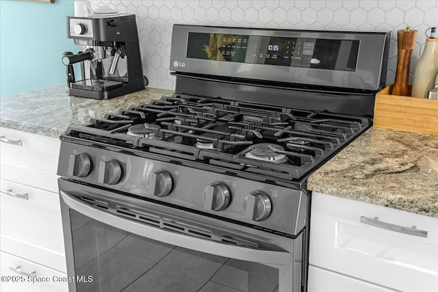 details featuring stainless steel gas range oven, light stone counters, and decorative backsplash