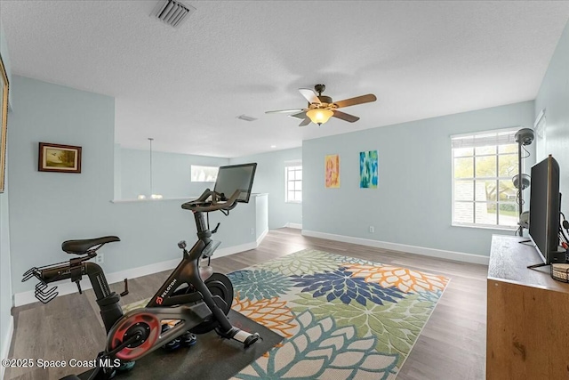 exercise area with visible vents, baseboards, a ceiling fan, light wood-style flooring, and a textured ceiling