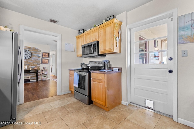 kitchen with light tile patterned floors, stainless steel appliances, a textured ceiling, and visible vents