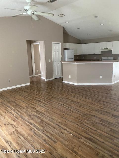 unfurnished living room featuring visible vents, baseboards, dark wood finished floors, a ceiling fan, and vaulted ceiling