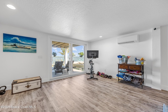 exercise area featuring a textured ceiling, recessed lighting, wood finished floors, baseboards, and a wall mounted AC