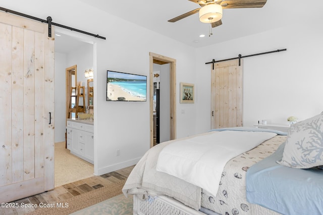 bedroom featuring a barn door, baseboards, connected bathroom, ceiling fan, and light wood-style flooring