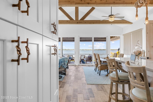 dining area with high vaulted ceiling, a water view, a ceiling fan, light wood-style floors, and beamed ceiling