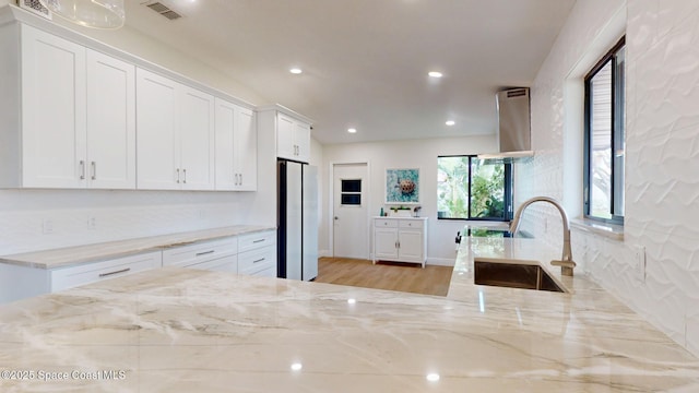 kitchen featuring light stone counters, a sink, freestanding refrigerator, and white cabinets