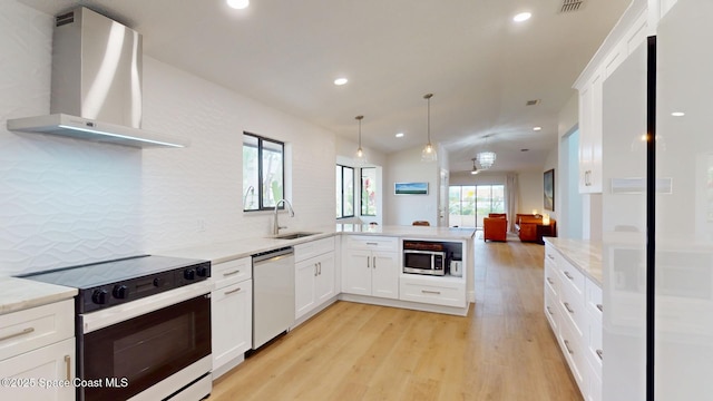 kitchen featuring a peninsula, a sink, light wood-style floors, appliances with stainless steel finishes, and wall chimney exhaust hood