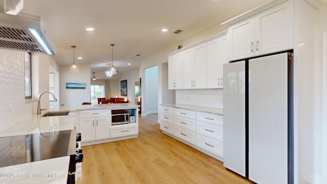 kitchen featuring a sink, visible vents, freestanding refrigerator, wall chimney exhaust hood, and stainless steel microwave