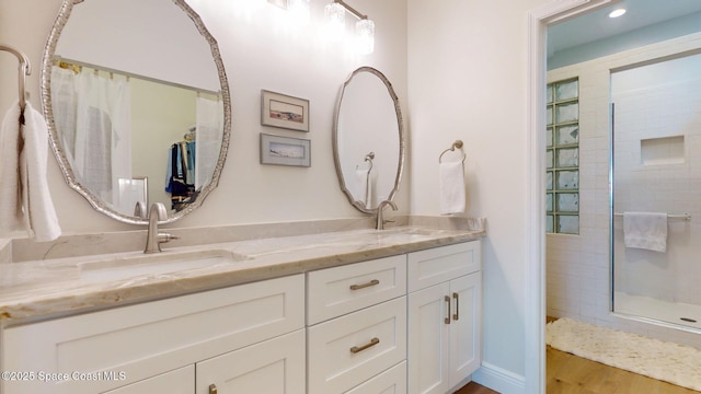 bathroom with double vanity, wood finished floors, a sink, and tiled shower