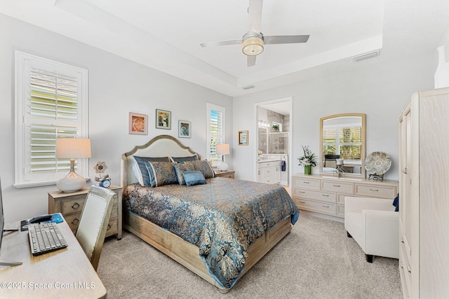 bedroom featuring light colored carpet, ensuite bathroom, a raised ceiling, and multiple windows