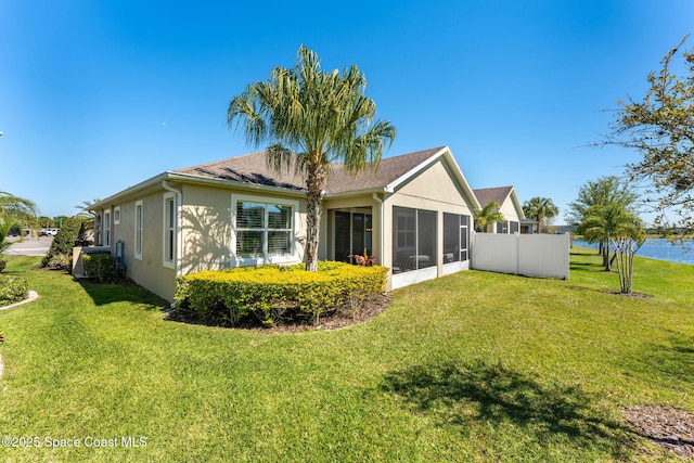 rear view of house with stucco siding, fence, a yard, and a sunroom