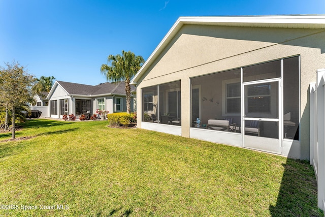 rear view of property with a lawn, a sunroom, and stucco siding