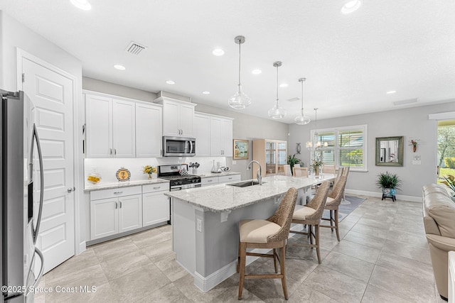 kitchen featuring visible vents, a breakfast bar area, decorative backsplash, appliances with stainless steel finishes, and a sink