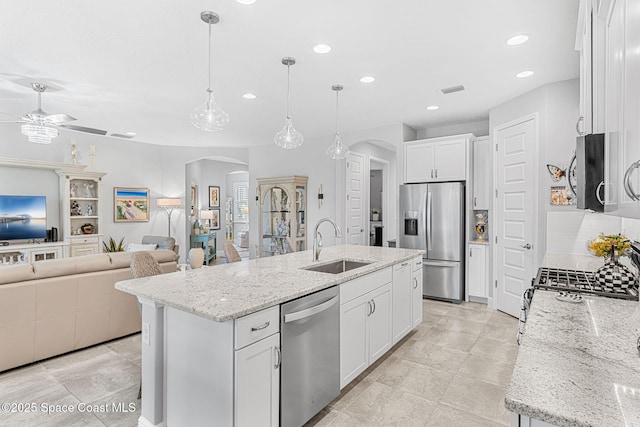 kitchen featuring a center island with sink, arched walkways, stainless steel appliances, a ceiling fan, and a sink