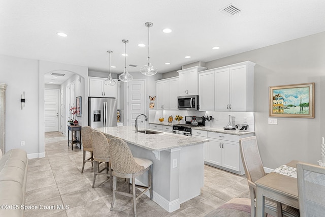 kitchen with arched walkways, a sink, decorative backsplash, stainless steel appliances, and a kitchen bar