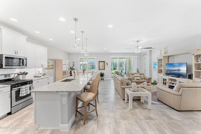 kitchen with open floor plan, a breakfast bar, decorative backsplash, stainless steel appliances, and a sink