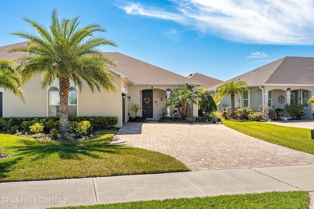 view of front of property with stucco siding, decorative driveway, and a front lawn