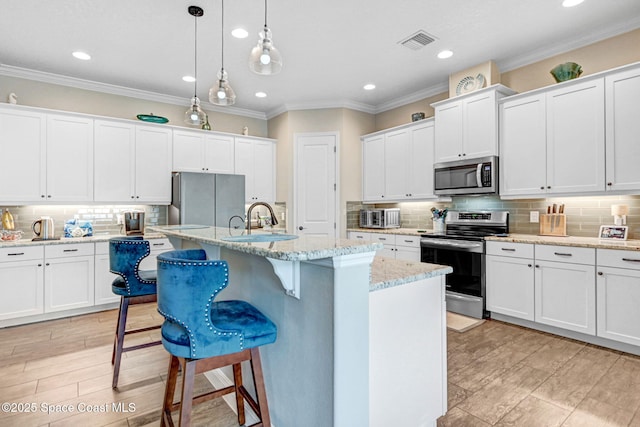 kitchen featuring visible vents, a sink, stainless steel appliances, white cabinetry, and a kitchen bar