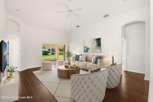 living area featuring wood finished floors, ceiling fan, arched walkways, baseboards, and a towering ceiling