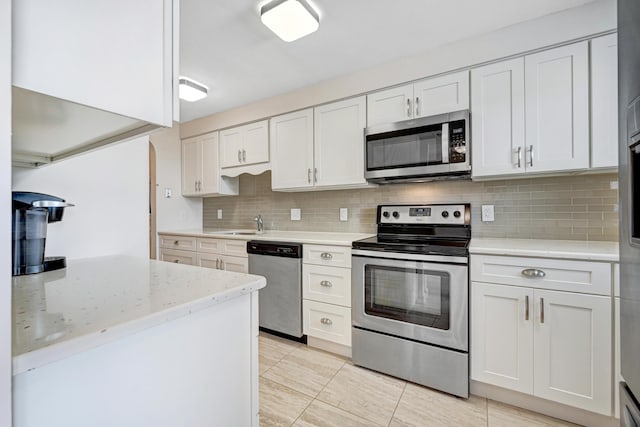 kitchen featuring decorative backsplash, appliances with stainless steel finishes, white cabinetry, a sink, and light stone countertops