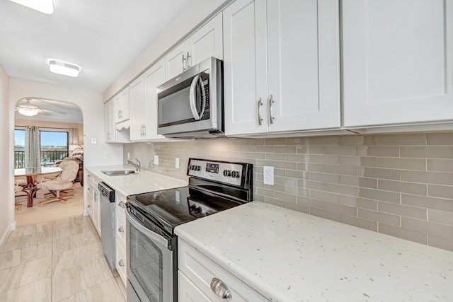 kitchen featuring stainless steel appliances, arched walkways, white cabinetry, and backsplash