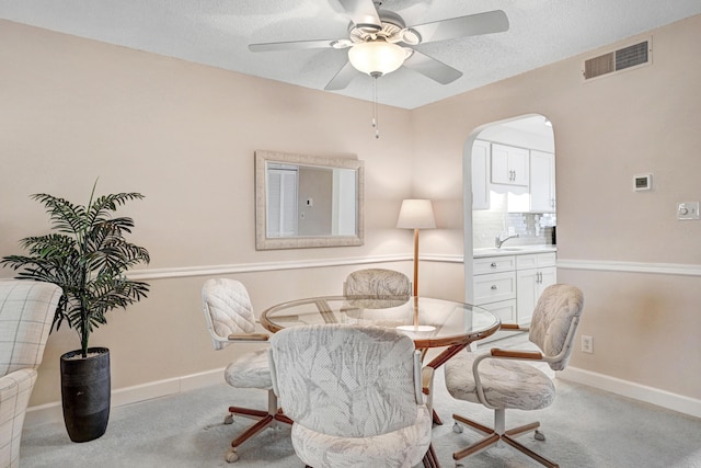 carpeted dining area with arched walkways, visible vents, a sink, and baseboards