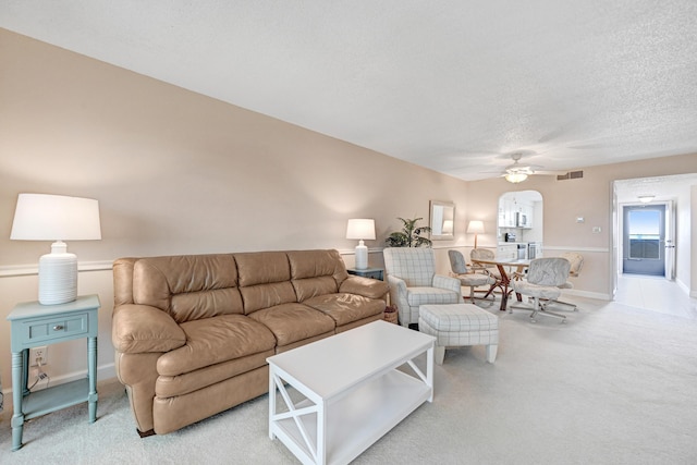 living room featuring light colored carpet, visible vents, ceiling fan, a textured ceiling, and baseboards