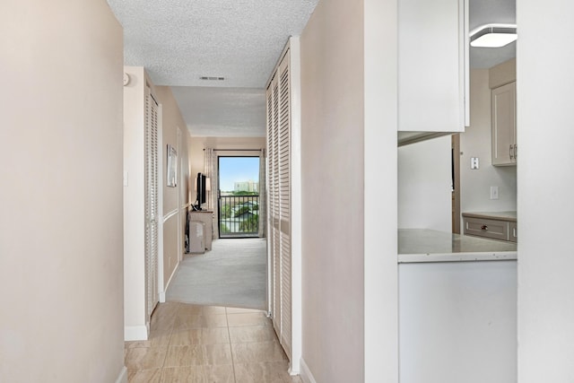 hall featuring light tile patterned floors, visible vents, light carpet, a textured ceiling, and baseboards