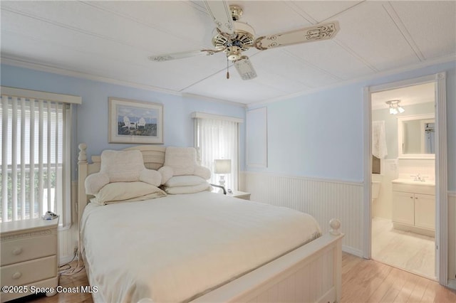 bedroom featuring ceiling fan, light wood-style flooring, a sink, wainscoting, and ensuite bath