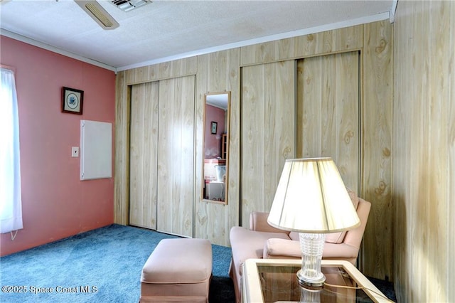 sitting room with a textured ceiling, wood walls, visible vents, ornamental molding, and carpet