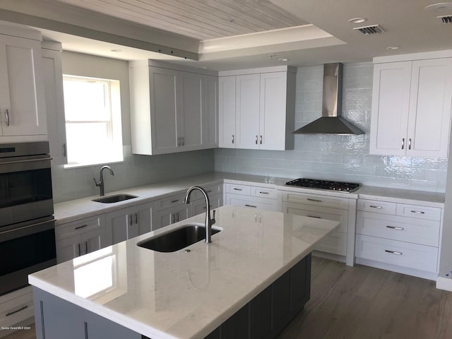 kitchen featuring double oven, black gas stovetop, wall chimney exhaust hood, and a sink