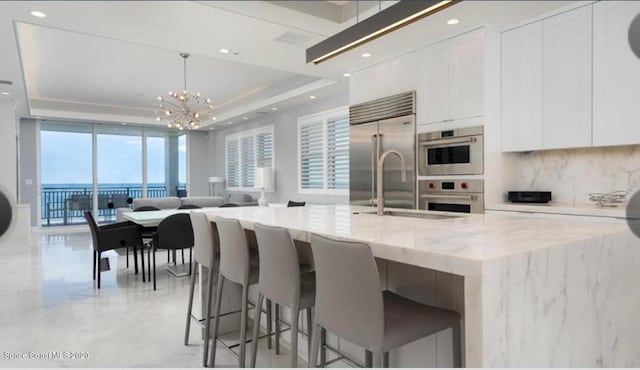 kitchen with white cabinets, open floor plan, appliances with stainless steel finishes, a raised ceiling, and tasteful backsplash