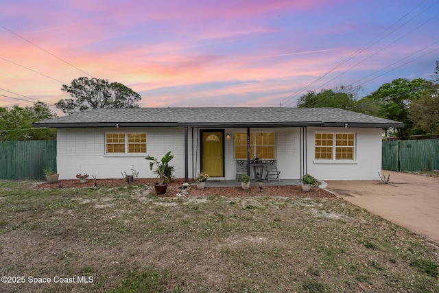 ranch-style house featuring a porch, concrete block siding, fence, and a shingled roof