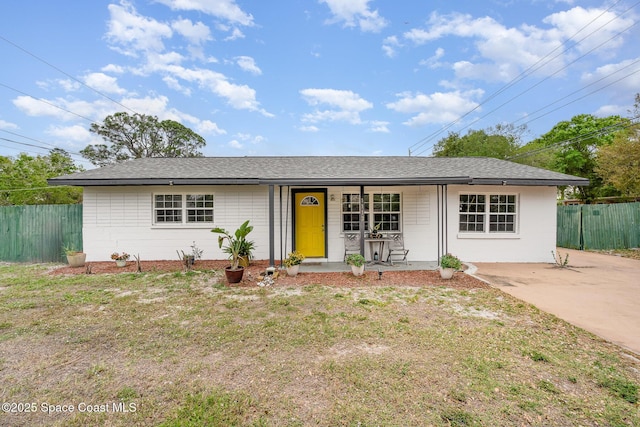 ranch-style home featuring covered porch, a shingled roof, concrete block siding, and fence