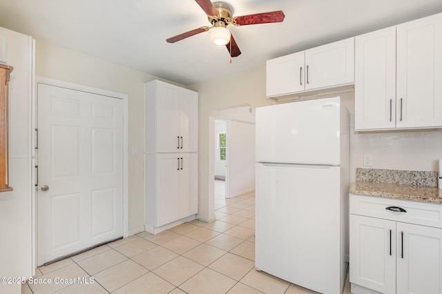 kitchen featuring light tile patterned floors, white cabinets, ceiling fan, light stone counters, and freestanding refrigerator