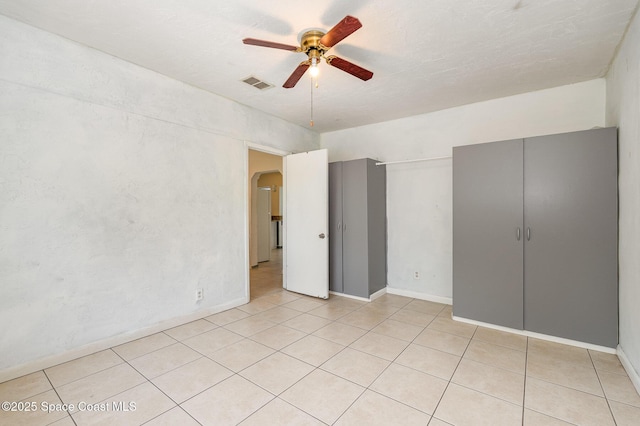 unfurnished bedroom featuring light tile patterned floors, visible vents, arched walkways, baseboards, and ceiling fan