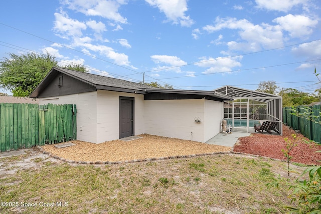 back of house with a pool, concrete block siding, a fenced backyard, and a lanai