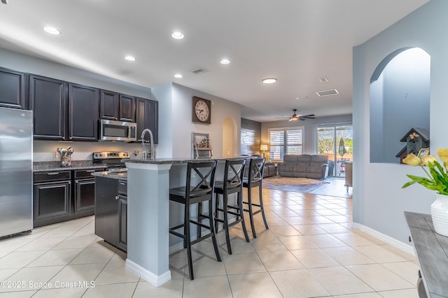 kitchen featuring light tile patterned floors, a breakfast bar area, stainless steel appliances, visible vents, and dark stone countertops