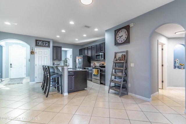 kitchen featuring stainless steel appliances, arched walkways, a kitchen bar, and light tile patterned floors