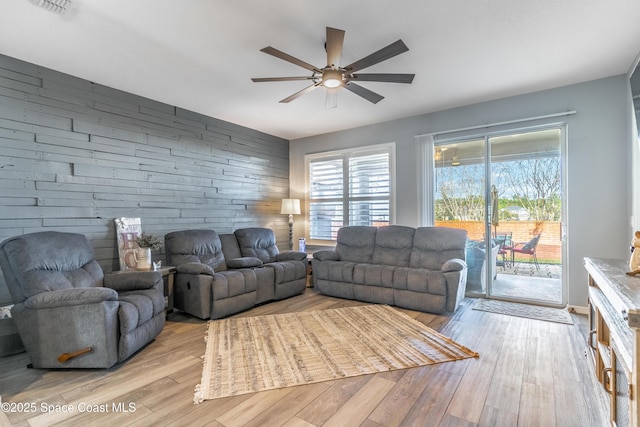 living room featuring ceiling fan, an accent wall, wood walls, and light wood-style flooring