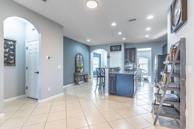 kitchen featuring light tile patterned floors, arched walkways, a kitchen breakfast bar, and freestanding refrigerator