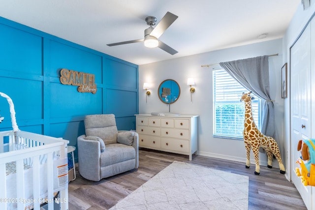 bedroom featuring a nursery area, ceiling fan, baseboards, and wood finished floors