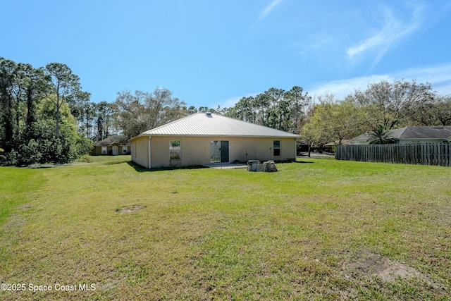 back of property with metal roof, a yard, and fence