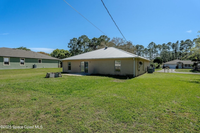 back of property with cooling unit, metal roof, a lawn, and a patio