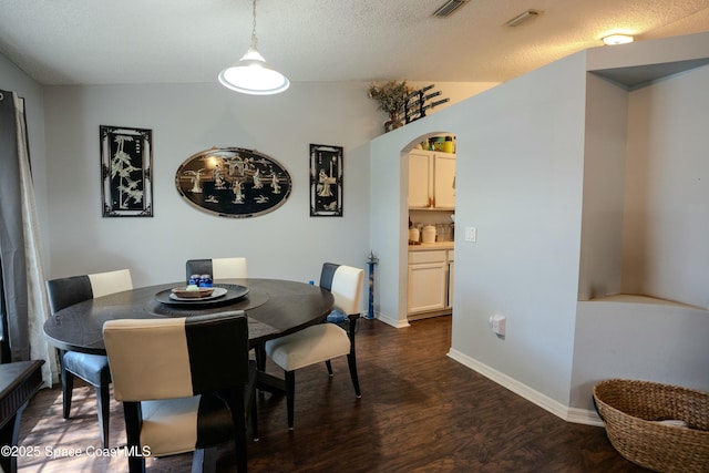 dining room featuring arched walkways, dark wood-style flooring, visible vents, a textured ceiling, and baseboards