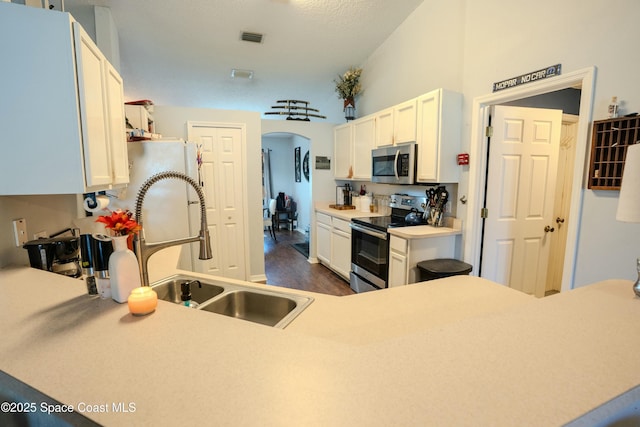 kitchen with arched walkways, appliances with stainless steel finishes, a sink, and white cabinets