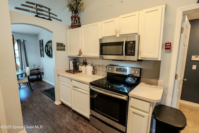 kitchen featuring arched walkways, white cabinets, dark wood-style floors, stainless steel appliances, and light countertops