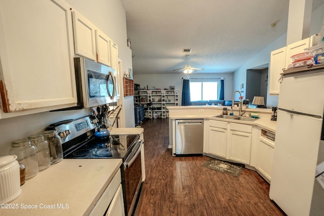 kitchen featuring dark wood-type flooring, a peninsula, stainless steel appliances, light countertops, and a sink