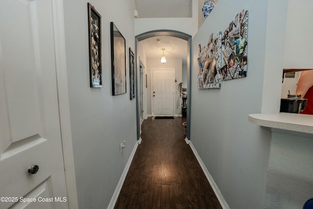 corridor with arched walkways, dark wood-style flooring, and baseboards