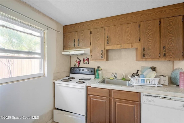 kitchen with white appliances, brown cabinetry, under cabinet range hood, and a sink